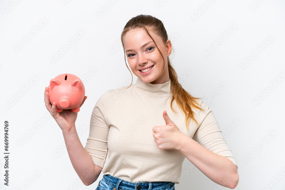 Young caucasian girl holding a piggybank isolated on white background with thumbs up because something good has happened Young caucasian girl holding a piggybank isolated on white background with thumbs up because something good has happened
