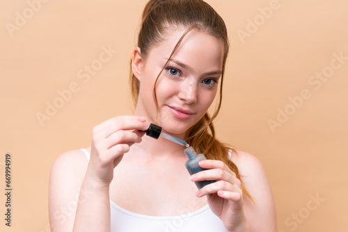 Young caucasian girl isolated on beige background holding a serum. Close up portrait