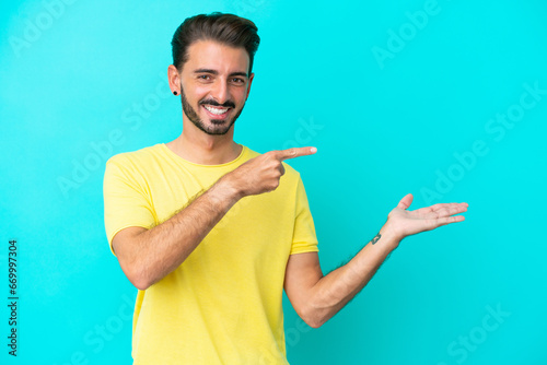 Young caucasian man isolated on blue background holding copyspace imaginary on the palm to insert an ad