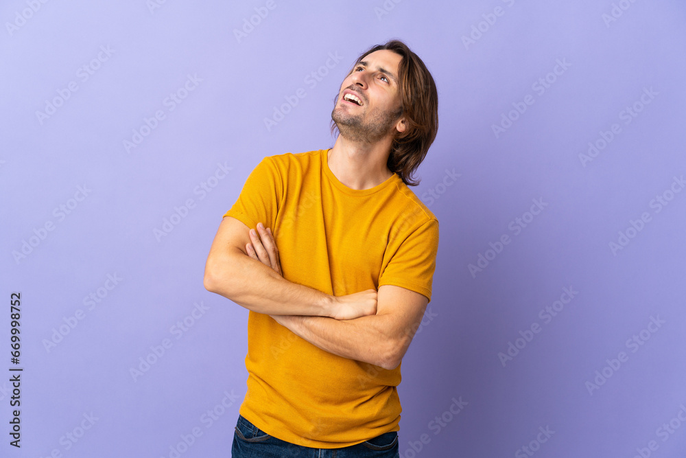 Young handsome man isolated on purple background looking up while smiling Young handsome man isolated on purple background looking up while smiling