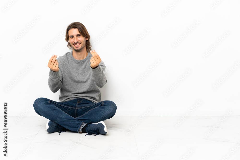 Young handsome man sitting on the floor over isolated background making money gesture Young handsome man sitting on the floor over isolated background making money gesture