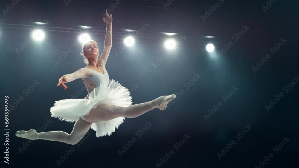 Graceful Ballet Dancer Performs a Powerful Split Leap During Her Act. Young Female Practicing in Striking Beautiful Dress in a Dark Room. Cinematic Super Slow Motion Speed Ramp Footage Graceful Ballet Dancer Performs a Powerful Split Leap During Her Act. Young Female Practicing in Striking Beautiful Dress in a Dark Room. Cinematic Super Slow Motion Speed Ramp Footage