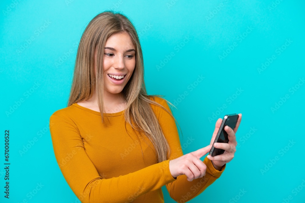 Young caucasian woman isolated on blue background sending a message or email with the mobile