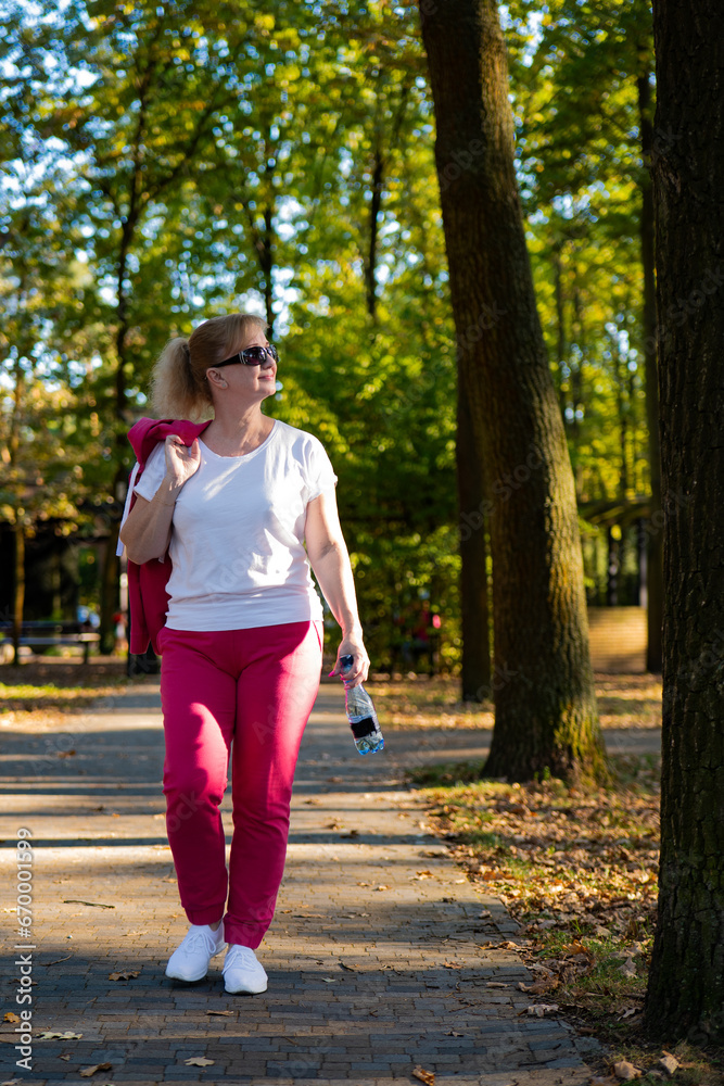 Woman on a walk in the park. Blonde girl in safety glasses. Woman in a red tracksuit, woman jogging in park