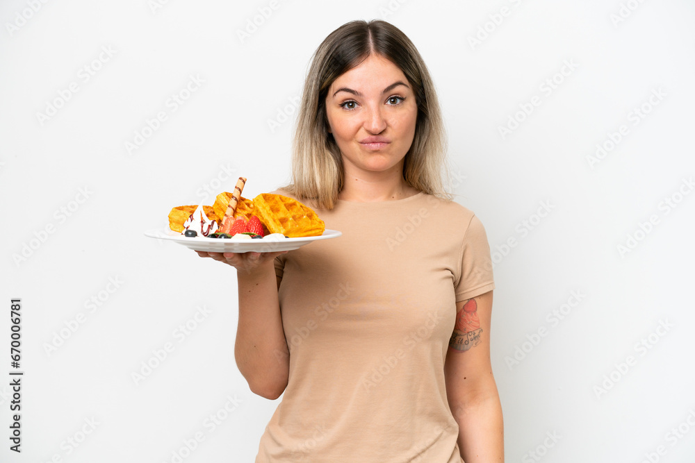 Young Rumanian woman holding waffles isolated on white background with sad expression