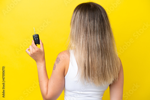 Young woman holding car keys isolated on yellow background in back position