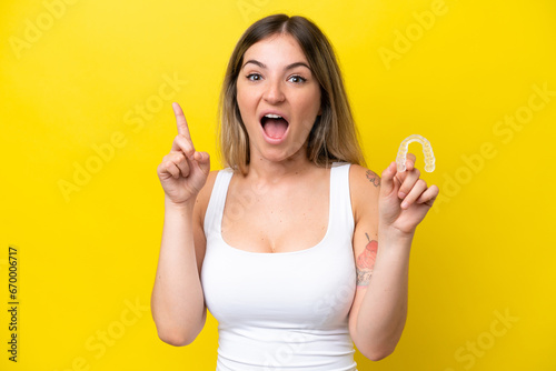 Young Rumanian woman holding envisaging isolated on yellow background pointing up a great idea