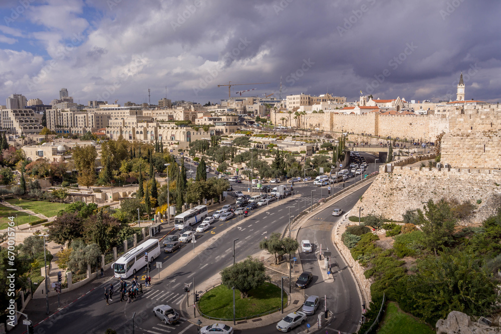 The car traffic on the junction (Hebron road and Yitzhak Kariv street) at Jerusalem downtown, with green parks, shopping malls, hotels, old town walls and towers, in Israel.