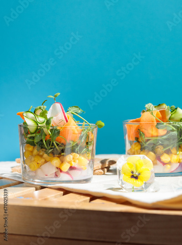Healthy salad of fresh vegetables, corn and microgreens in a glass bowl, on a blue background. Vertical frame.