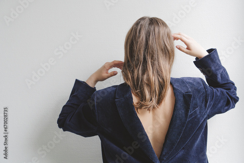 Brunette teenage girl wearing navy blue blazer backwards in front of wall photo
