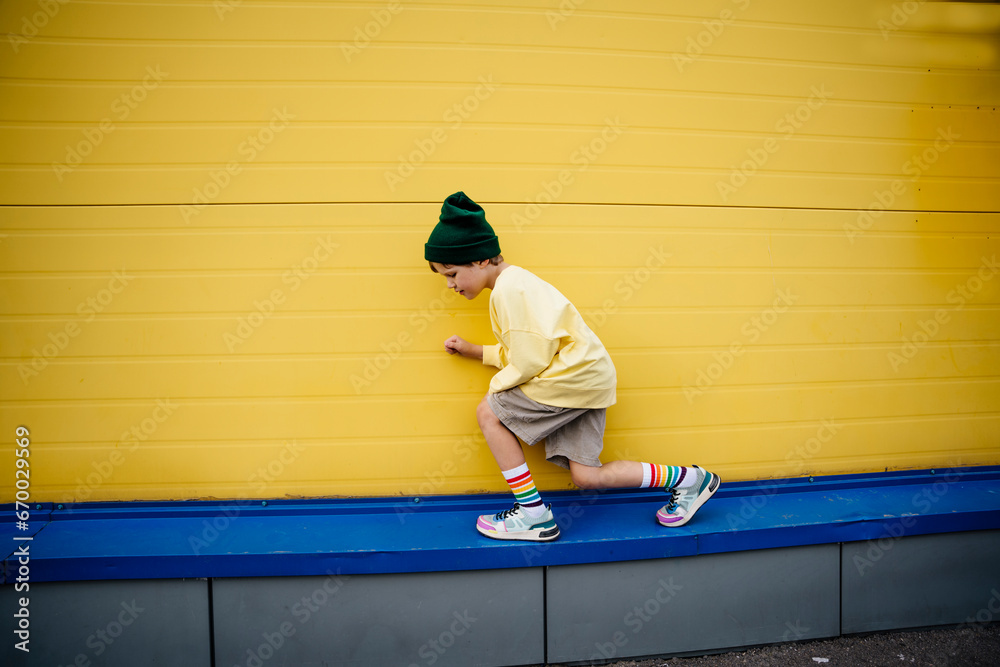 Playful boy wearing sweatshirt crouching in front of yellow wall Playful boy wearing sweatshirt crouching in front of yellow wall