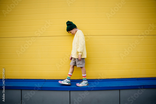 Boy wearing sweatshirt looking down and walking by yellow wall