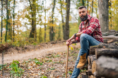 A hipster lumberjack relaxes on the pile of freshly cut logs, pausing for a portrait.
