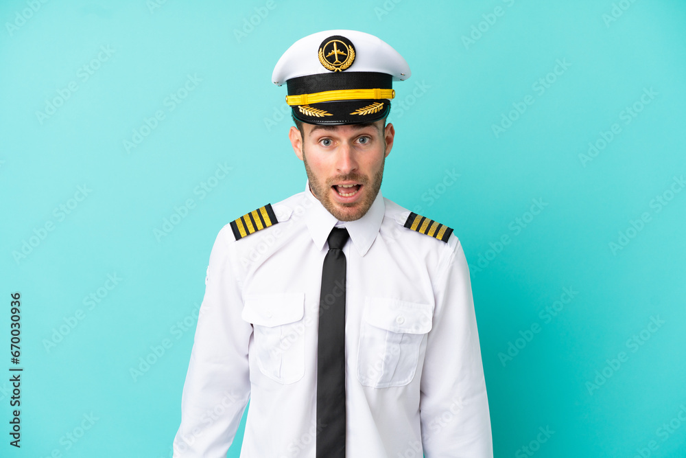 Airplane caucasian pilot isolated on blue background with surprise facial expression Airplane caucasian pilot isolated on blue background with surprise facial expression