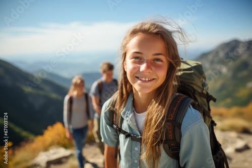 Portrait of smiling teen girl posing on mountain with her family in background, Happy teenager hiking with family in summer, Adolescence and family weekend concept