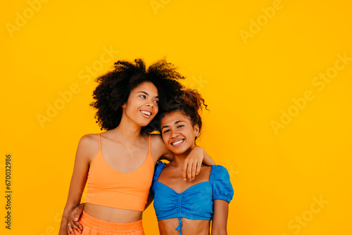 Woman with arm around smiling friend against yellow background photo