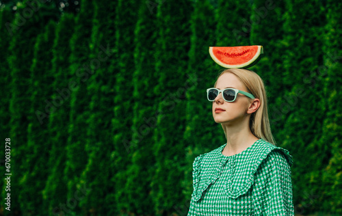 Woman wearing sunglasses standing with watermelon on head in garden