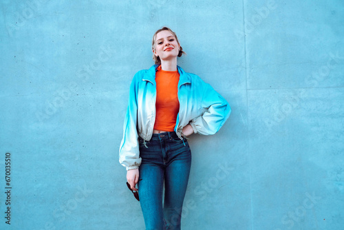 Smiling young woman with hand on hip standing in front of blue wall photo
