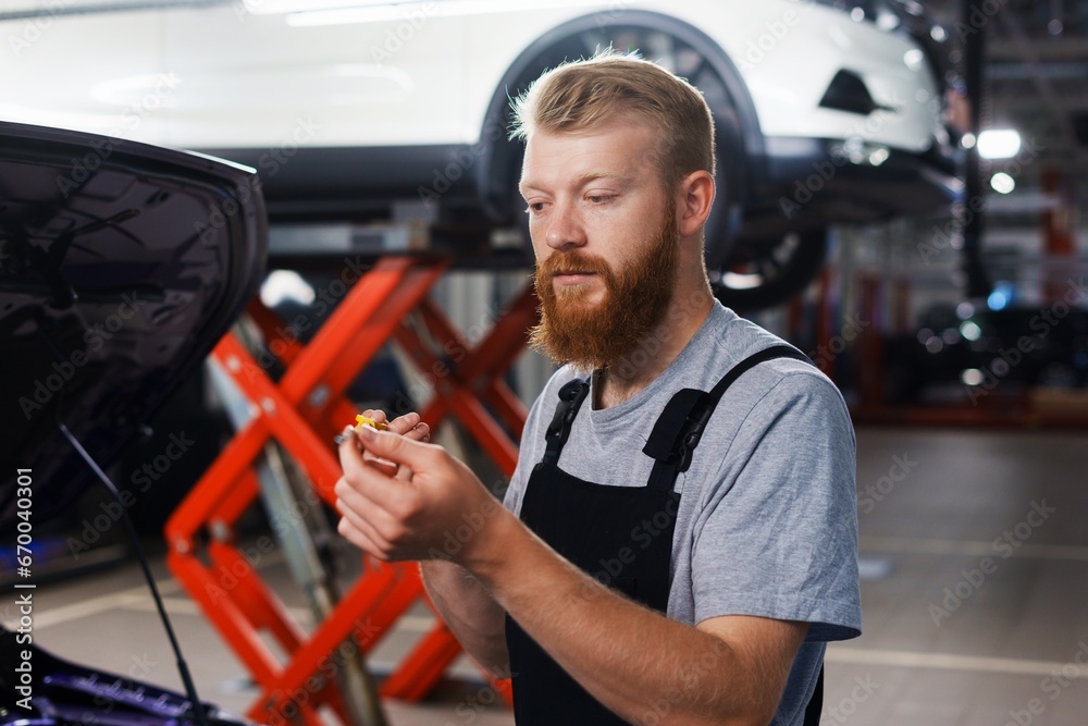 A car service worker checks the oil level in the engine. A man in uniform is looking at an oil dipstick. Timely checking of liquids in the car A car service worker checks the oil level in the engine. A man in uniform is looking at an oil dipstick. Timely checking of liquids in the car