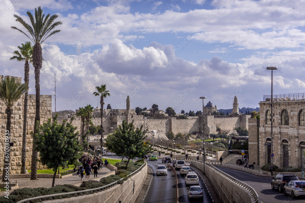 Naklejka premium The road traffic on Jerusalem highway going along the walls of the Old town, with the palm trees, and cloudy sky, in Israel.