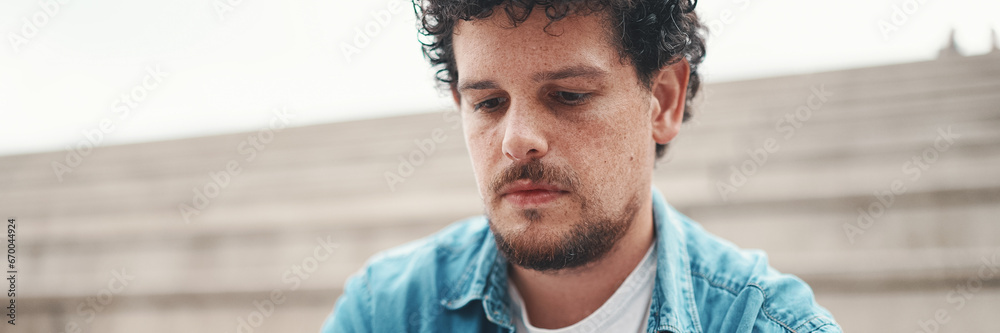 Obraz premium young bearded man in denim shirt sitting on high steps and using mobile phone. Man playing on smartphone