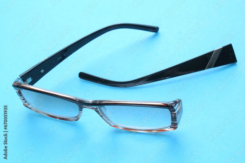 Old broken eyeglasses with damaged legs on blue background. Poor eyesight. Reuse and repair concept. Idea of health. Failure optic eyewear. Breakage of vision correction glasses. Close up, flat lay Old broken eyeglasses with damaged legs on blue background. Poor eyesight. Reuse and repair concept. Idea of health. Failure optic eyewear. Breakage of vision correction glasses. Close up, flat lay