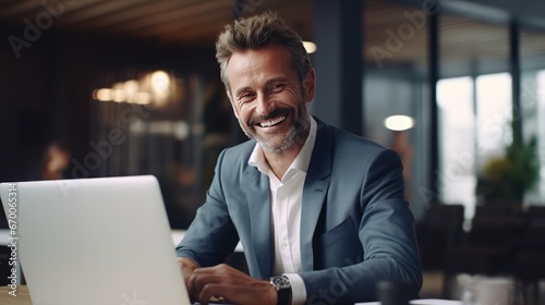 Mature smiling businessman working on laptop computer in office.
