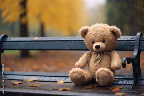 Lonely teddy bear in warm clothes on wooden bench under the rain