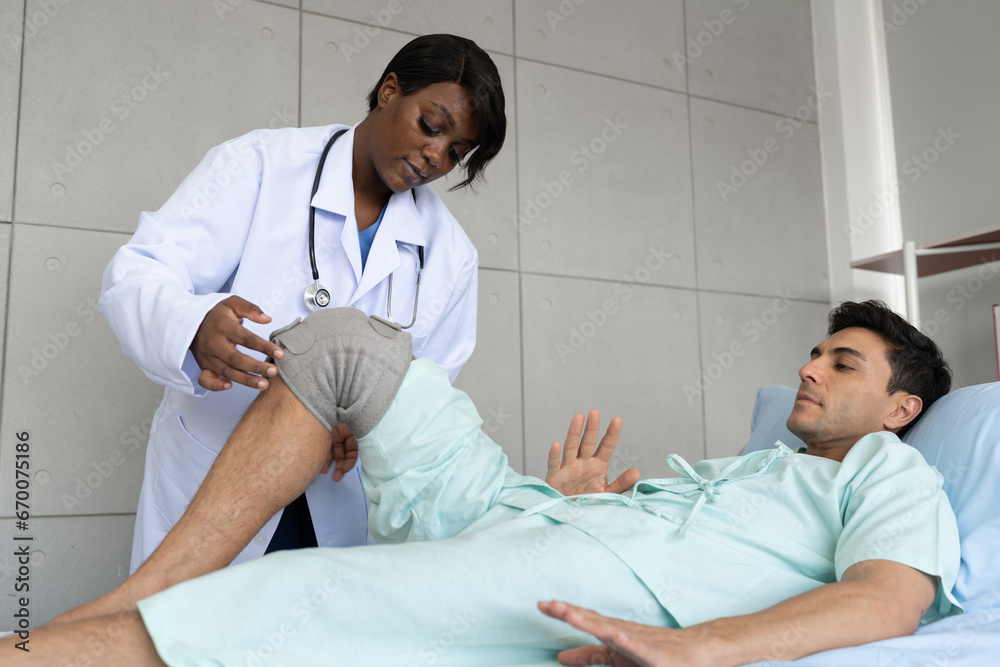 Obraz premium African American Doctor or Physiotherapist working examining treating of caucasian patient, leg stretching and exercise with wearing knee orthoses, in clinic 