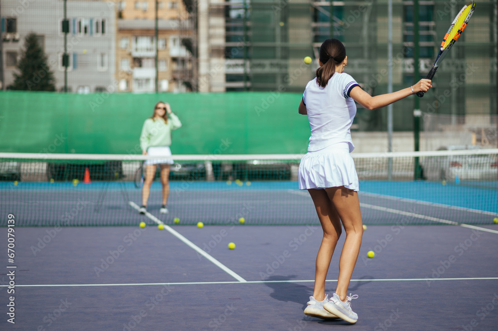 The coach trains the student to hit balls. Two women practice playing tennis on the court. Tennis training of two women.