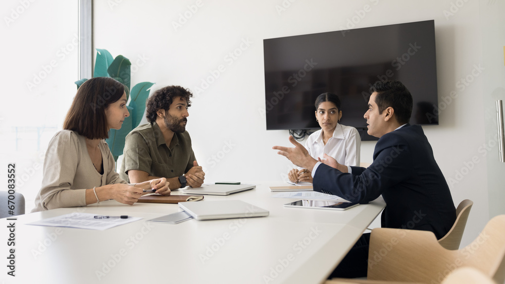 Serious diverse business colleagues discussing work on project, management strategy, meeting at table in boardroom. Young Indian leader woman holding negotiation of partners Serious diverse business colleagues discussing work on project, management strategy, meeting at table in boardroom. Young Indian leader woman holding negotiation of partners