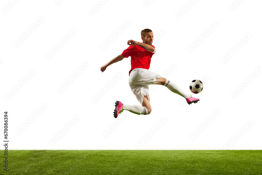 Full length portrait of professional soccer player kicking ball in motion against white background on green grass. Looks extremely motivated.