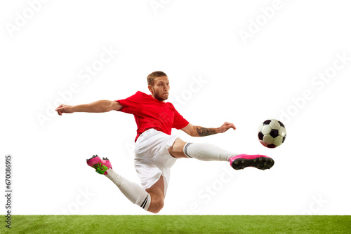 Young soccer soccer player looks confident practicing kicking ball in motion against white background on green grass. Football school.
