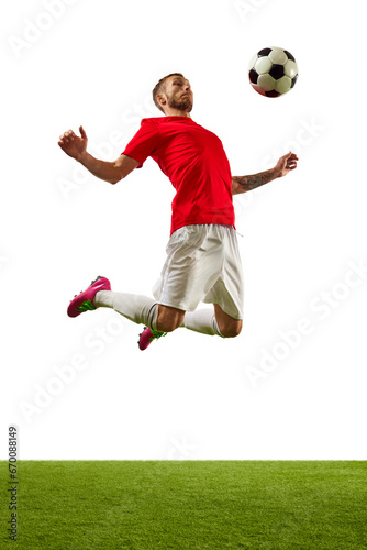 Young man, professional player in red sportwear and boots performing football tricks against white background with green grass. © Lustre