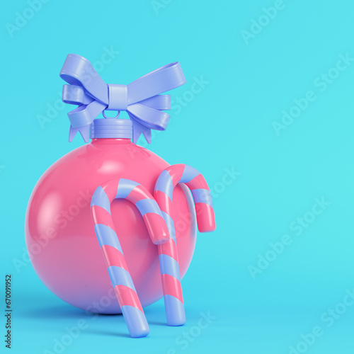 Fotografija Pink christmas bauble with a bow and teo candy cane on bright blue background in