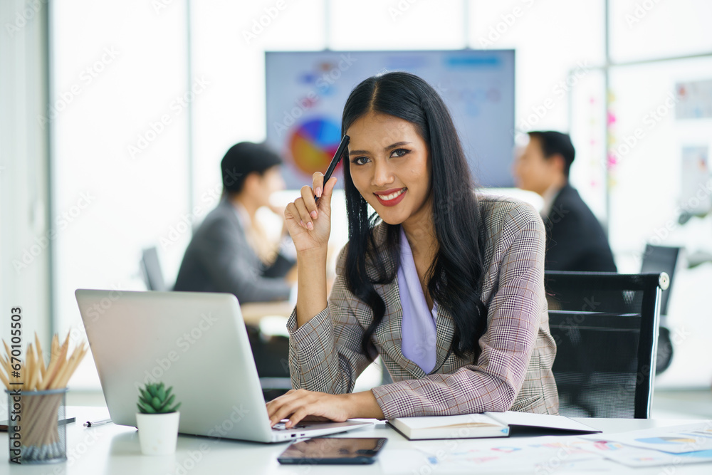 Happy young confident businesswoman sitting at the office table with group of colleagues Happy young confident businesswoman sitting at the office table with group of colleagues
