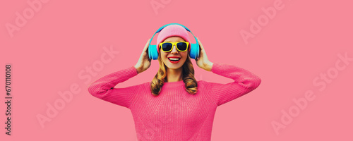 Portrait of happy smiling young woman with headphones listening to music wearing colorful pink sweater on studio background