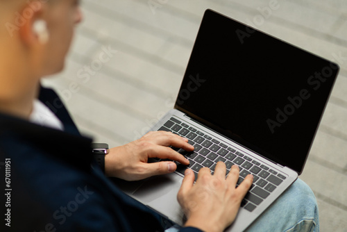 Busy young european man in wireless headphones work on laptop with empty screen
