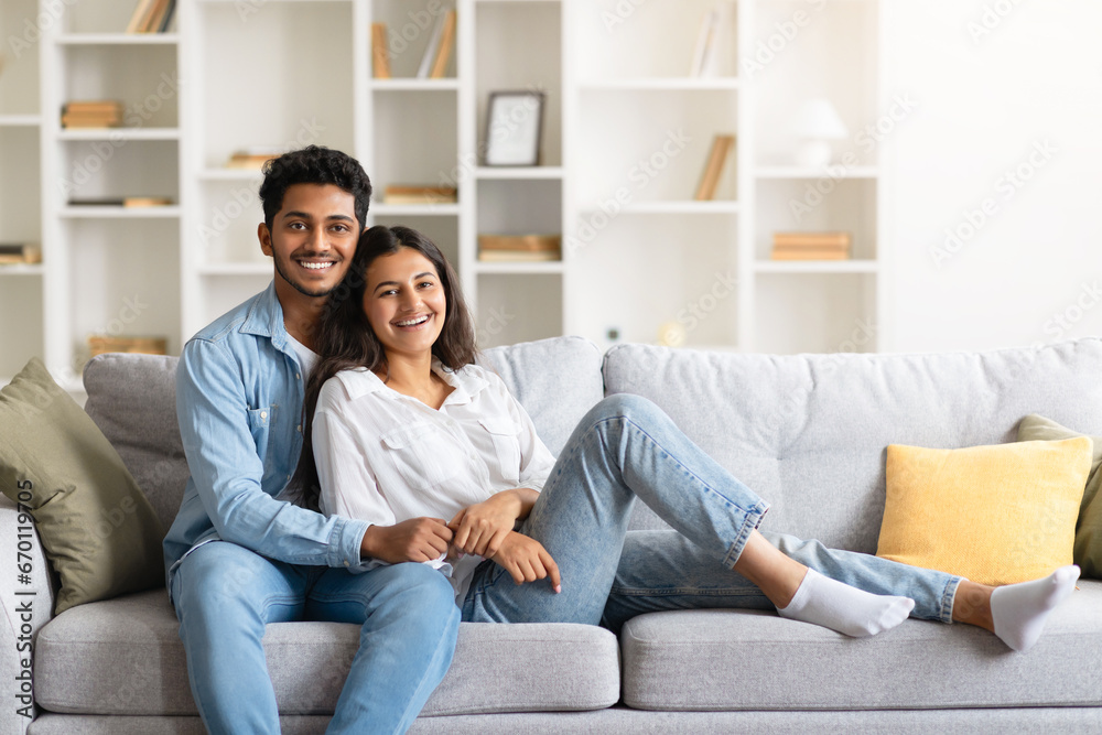 Relaxed indian couple sitting on a couch, embracing and smiling together at camera Relaxed indian couple sitting on a couch, embracing and smiling together at camera