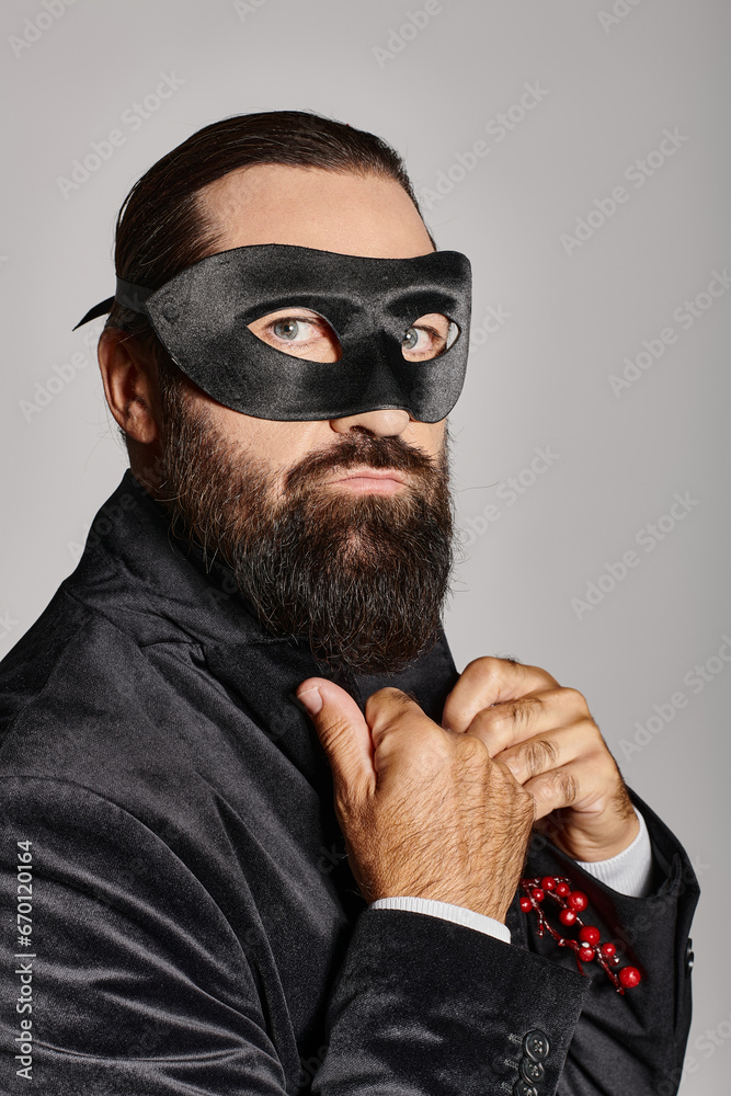 Obraz premium Christmas Masquerade, handsome bearded man in carnival mask and elegant suit on grey backdrop