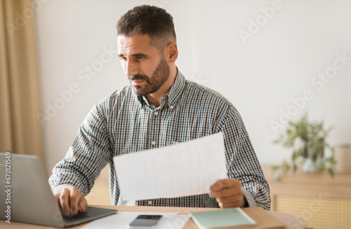 Entrepreneur reviewing paper and browsing on laptop at modern office