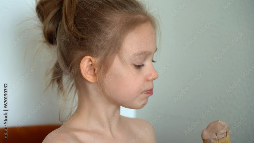 Little girl eats chocolate ice cream in waffle cone in kitchen at home. Child eats sweets