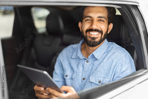 Happy eastern man in casual going by taxi, using tablet
