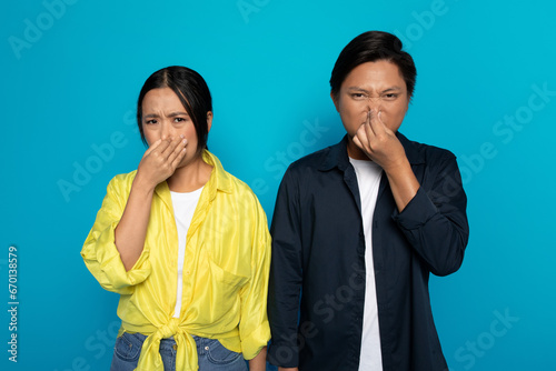 Obraz na plátně Upset sad millennial asian couple in casual covers nose with hands, suffers from