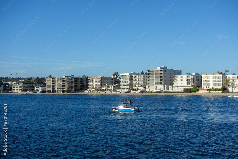 Motorboat moving leisurely thru warm waters of Mission Bay in front of resort style housing in San Diego, California