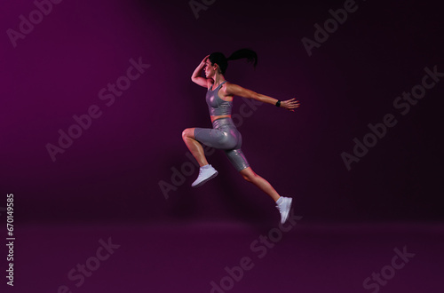 Side view of a young slim woman jumping against a magenta backdrop