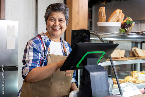 фотографія Gray-haired retired elderly business woman receives pension Standing in frontcash register counter, checking annual sales cafe's large volumes of coffee and bakery goods
