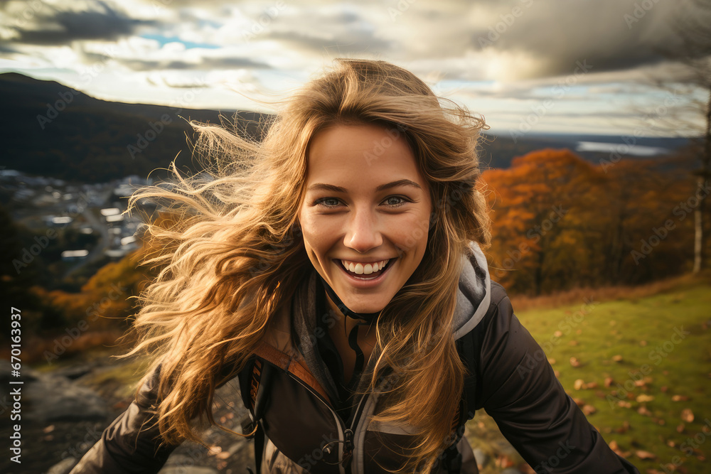 A joyful woman smiles against a breathtaking autumn backdrop, with windswept hair framing a scenic mountain view.