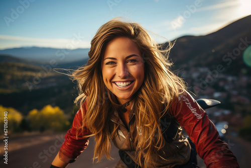 Radiant woman with windswept hair enjoys the sunset glow, overlooking a distant mountain town and open road. © apratim