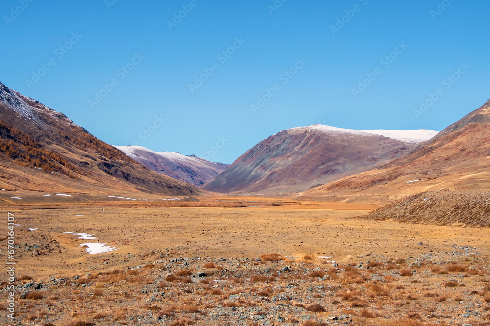 Desert landscape. Picturesque steppe autumn landscape with snow covered mountains, steppes with sparse vegetation on a background of blue sky.